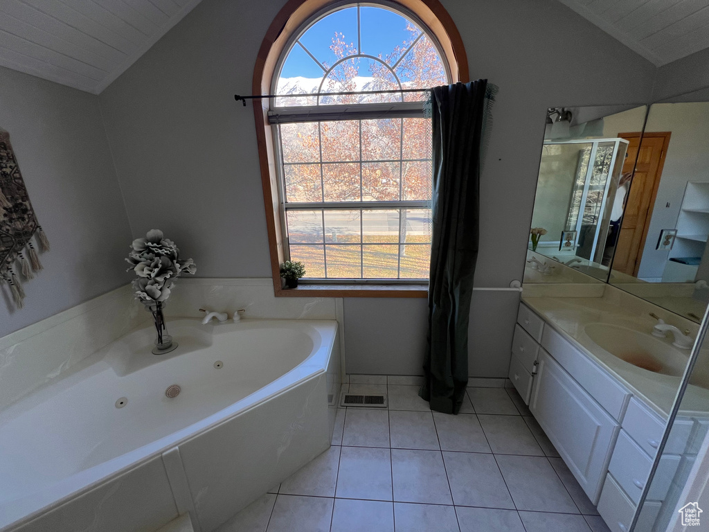 Bathroom featuring lofted ceiling, tile flooring, a wealth of natural light, and a bath to relax in