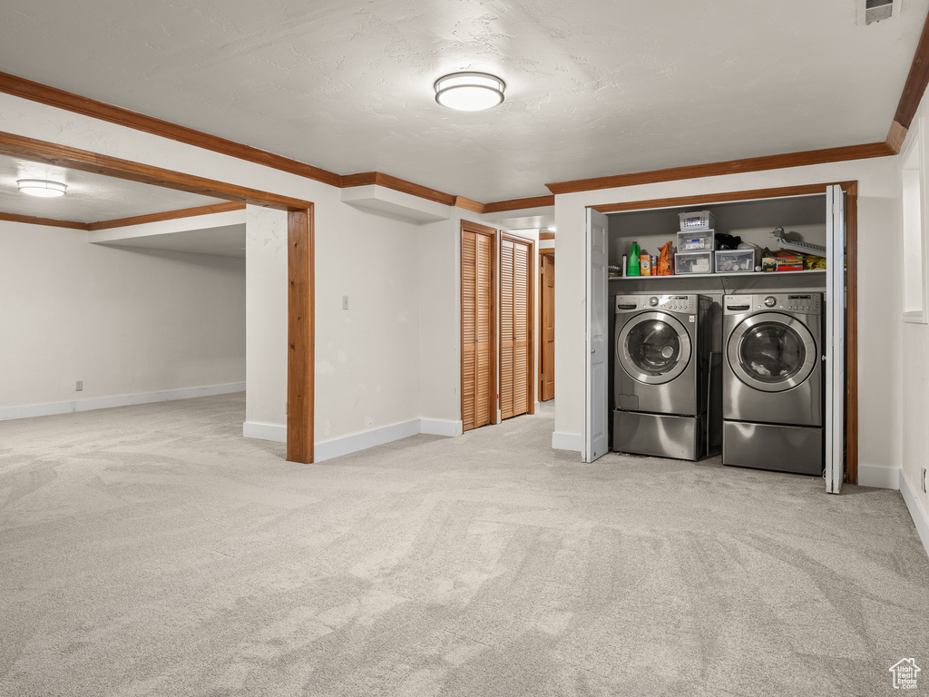 Clothes washing area featuring light carpet, ornamental molding, and separate washer and dryer