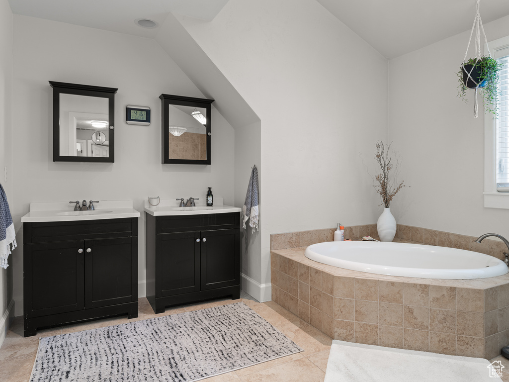 Bathroom featuring vanity with extensive cabinet space, tiled bath, tile floors, and vaulted ceiling