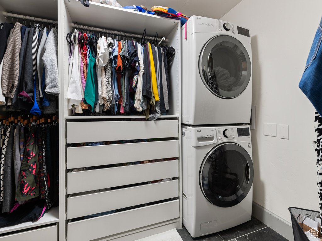 Laundry room with stacked washer and clothes dryer and dark tile flooring
