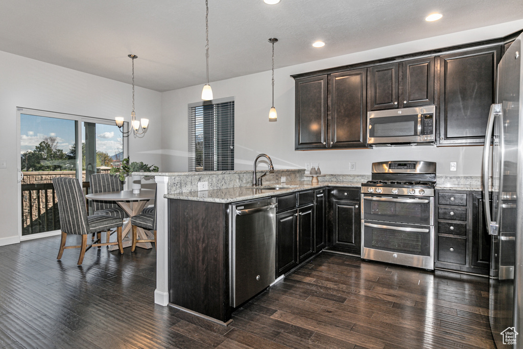 Kitchen featuring appliances with stainless steel finishes, light stone countertops, pendant lighting, and dark wood-type flooring