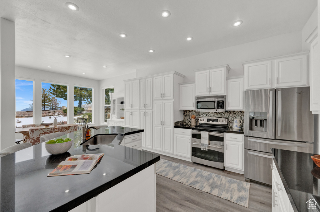 Kitchen featuring appliances with stainless steel finishes, sink, backsplash, white cabinetry, and light hardwood / wood-style flooring