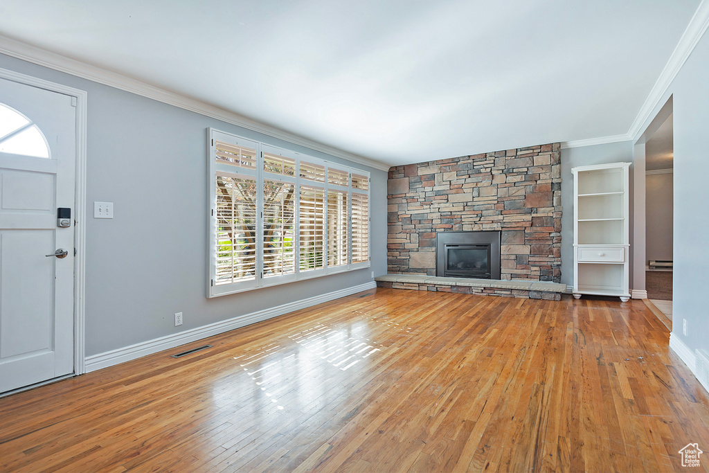 Unfurnished living room with crown molding, light wood-type flooring, baseboard heating, and a stone fireplace