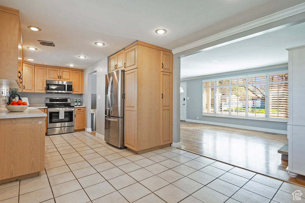 Kitchen featuring light brown cabinetry, crown molding, light tile floors, and stainless steel appliances