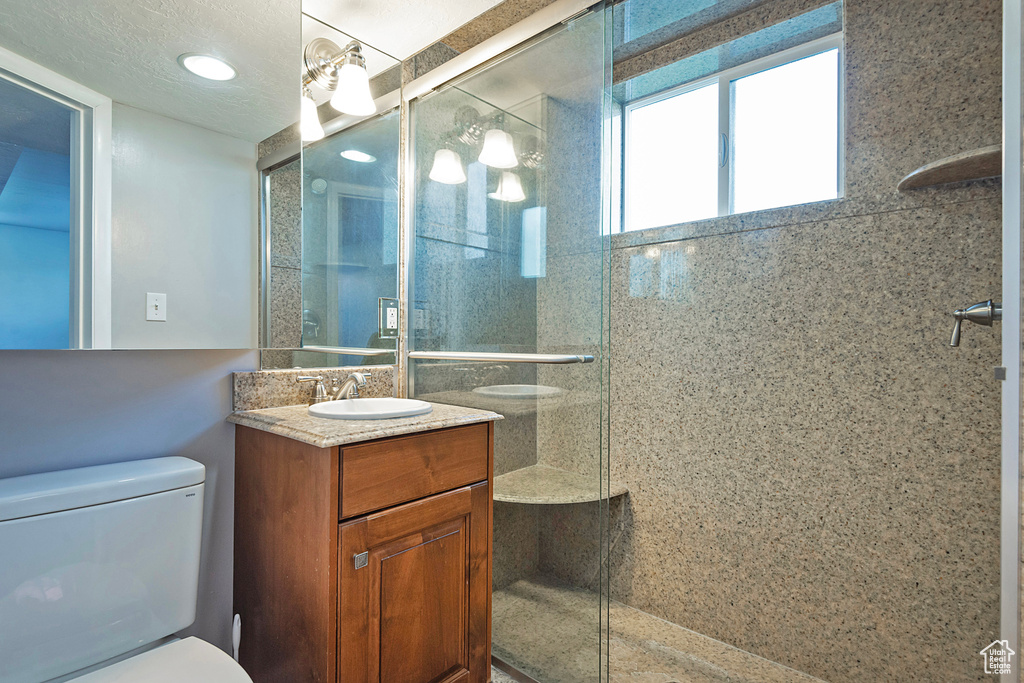 Bathroom featuring a shower with shower door, toilet, and large vanity