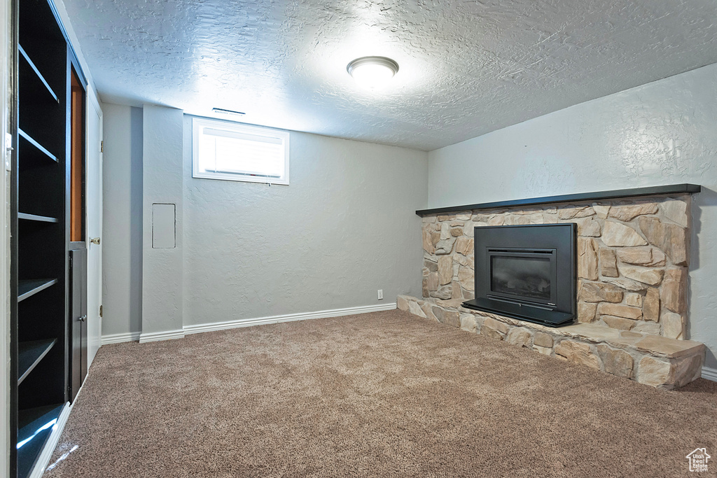 Unfurnished living room with a stone fireplace, a textured ceiling, and carpet floors