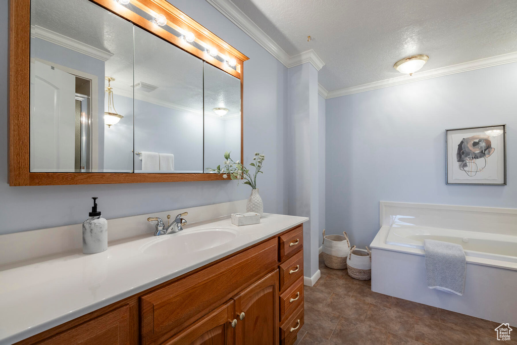 Bathroom with a textured ceiling, crown molding, tile floors, a bathtub, and vanity
