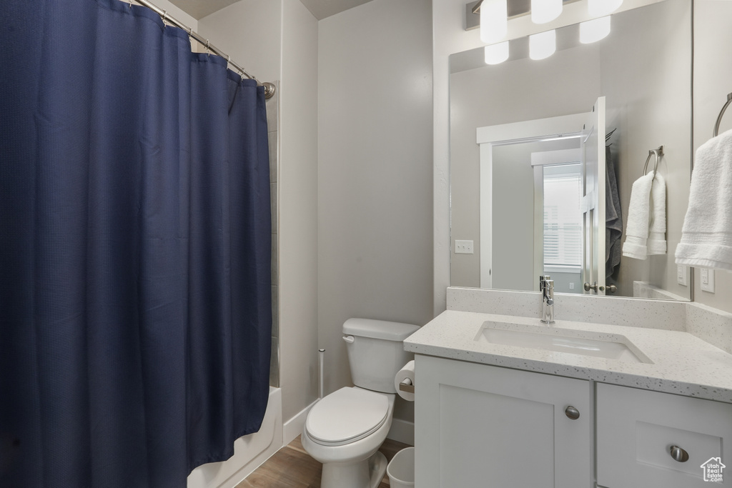 Full bathroom with hardwood / wood-style floors, shower / bath combo with shower curtain, toilet, and vanity