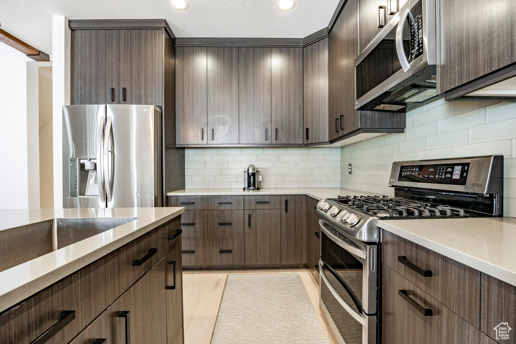 Kitchen with backsplash, dark brown cabinets, light hardwood / wood-style floors, and stainless steel appliances
