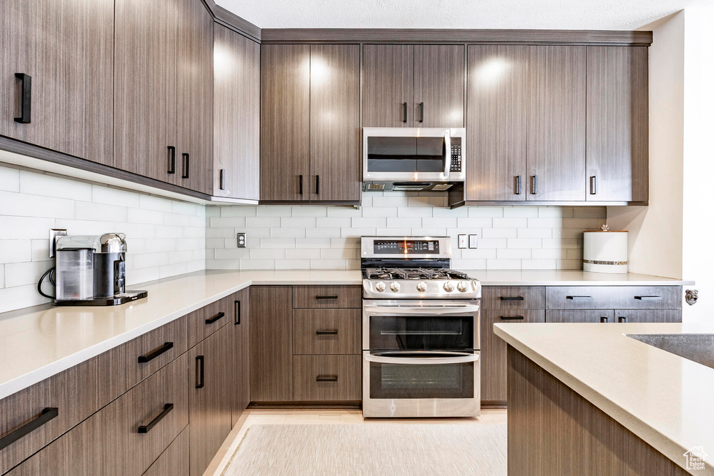 Kitchen with tasteful backsplash, appliances with stainless steel finishes, and dark brown cabinets