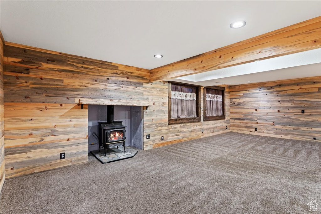 Unfurnished living room featuring a wood stove, dark carpet, and wooden walls