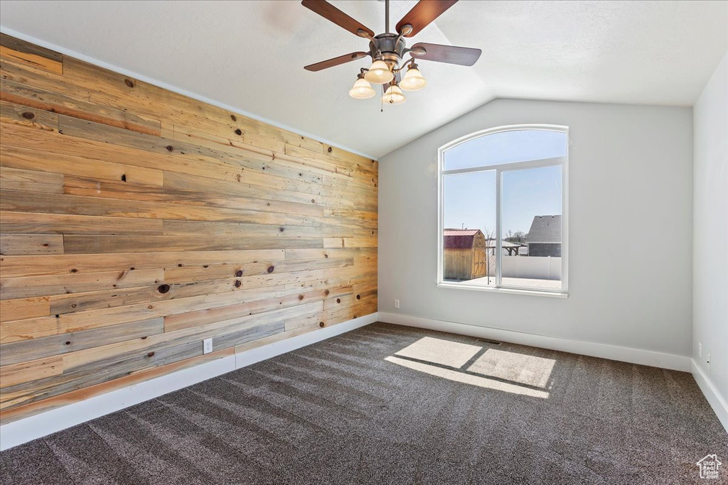 Spare room with lofted ceiling, ceiling fan, wood walls, and dark colored carpet