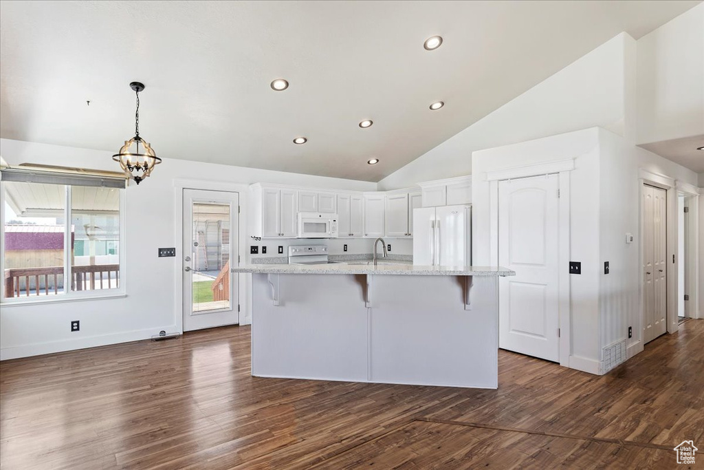 Kitchen featuring a kitchen bar, white appliances, an island with sink, and white cabinetry