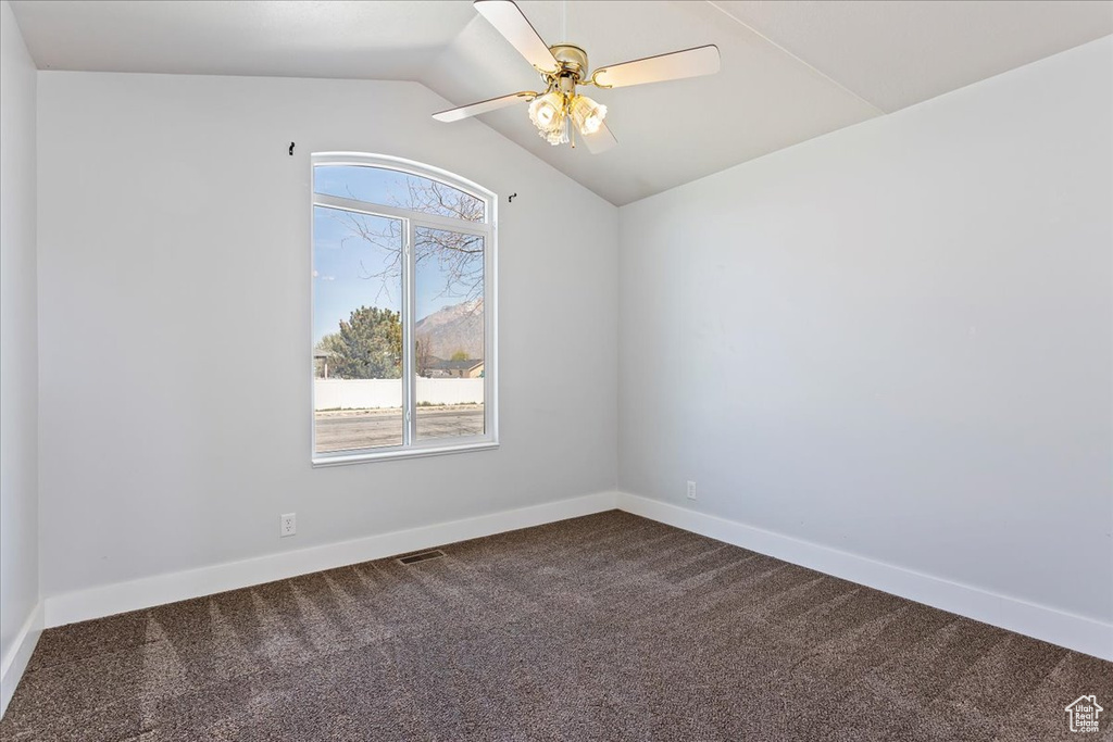Empty room featuring ceiling fan, a wealth of natural light, vaulted ceiling, and dark carpet