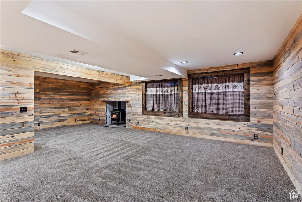 Unfurnished living room featuring dark colored carpet, wooden walls, and a wood stove