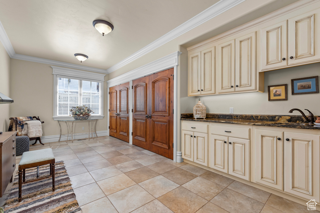 Kitchen featuring cream cabinets, dark stone countertops, sink, light tile floors, and ornamental molding