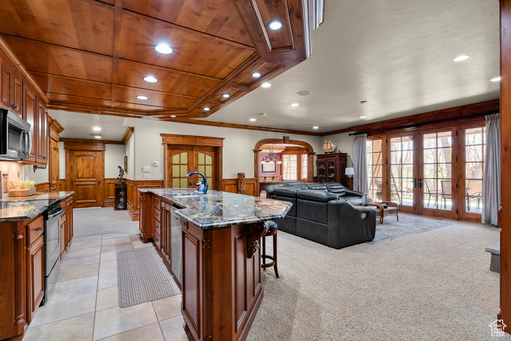 Kitchen with french doors, a center island with sink, dark stone counters, and electric stove