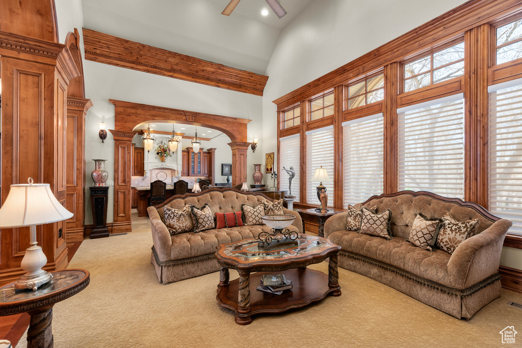 Living room with light colored carpet, ceiling fan, decorative columns, and a high ceiling