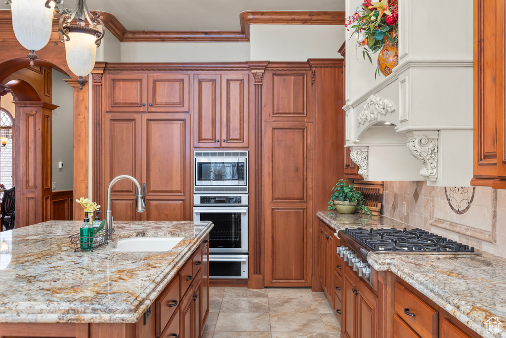 Kitchen featuring light stone counters, sink, backsplash, stainless steel appliances, and an island with sink