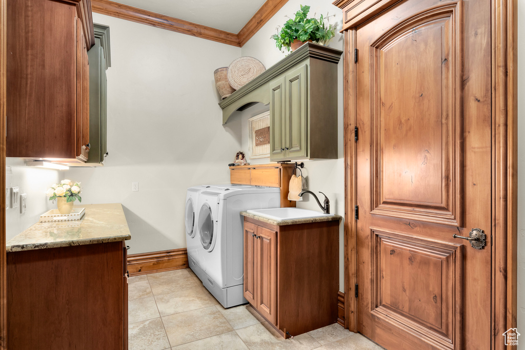 Clothes washing area featuring washer and dryer, cabinets, light tile floors, sink, and crown molding