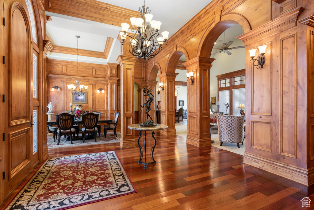Foyer with coffered ceiling, ceiling fan with notable chandelier, crown molding, dark hardwood / wood-style floors, and ornate columns