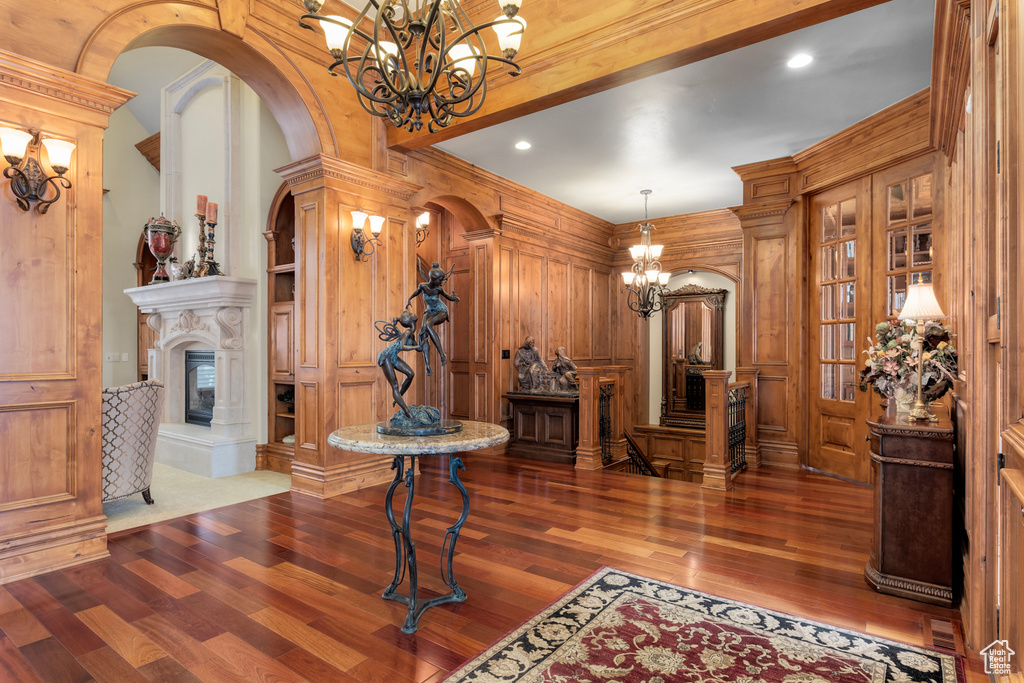 Foyer entrance featuring wooden walls, dark hardwood / wood-style flooring, ornate columns, and a notable chandelier