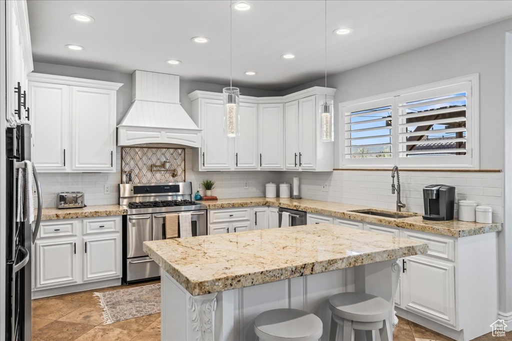 Kitchen featuring backsplash, premium range hood, stainless steel appliances, and white cabinetry