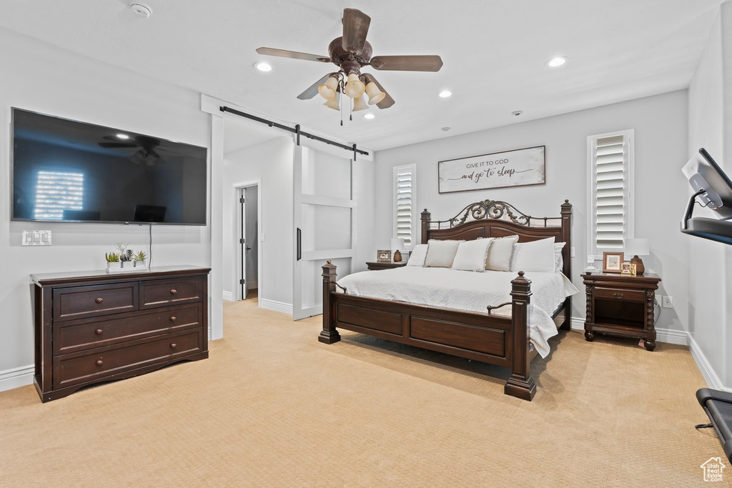 Bedroom featuring light colored carpet, ceiling fan, and a barn door