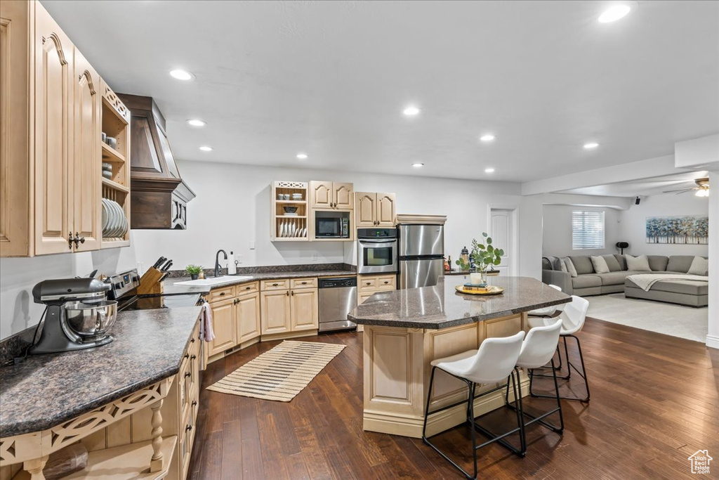 Kitchen featuring a kitchen bar, stainless steel appliances, dark hardwood / wood-style floors, sink, and a center island