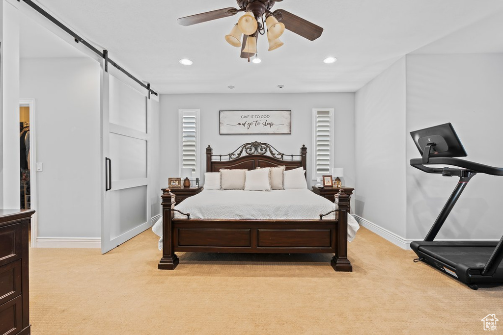 Bedroom with light colored carpet, ceiling fan, and a barn door