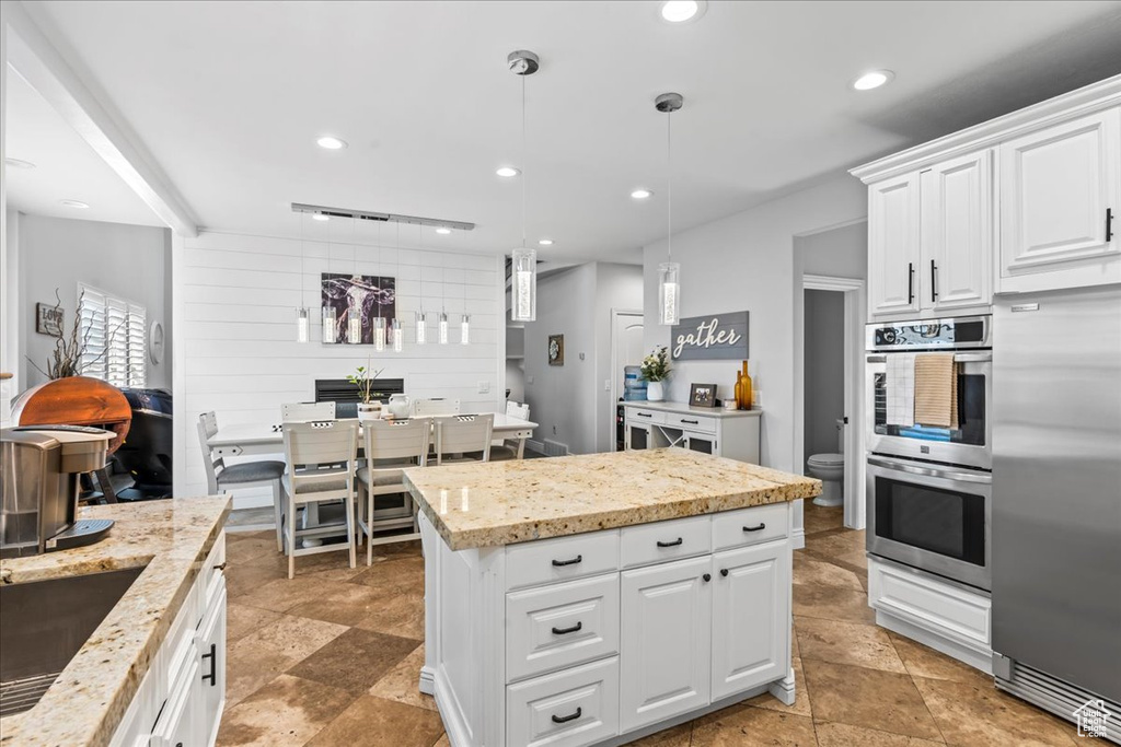 Kitchen featuring decorative light fixtures, light tile flooring, white cabinetry, appliances with stainless steel finishes, and a kitchen island