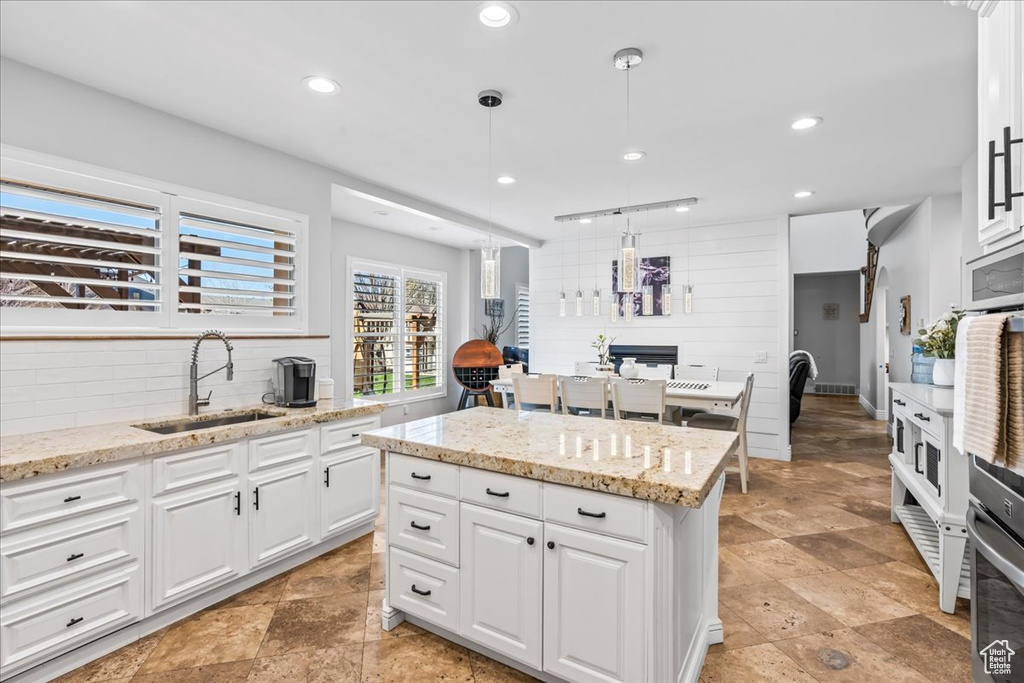 Kitchen with sink, white cabinetry, light tile floors, and decorative light fixtures