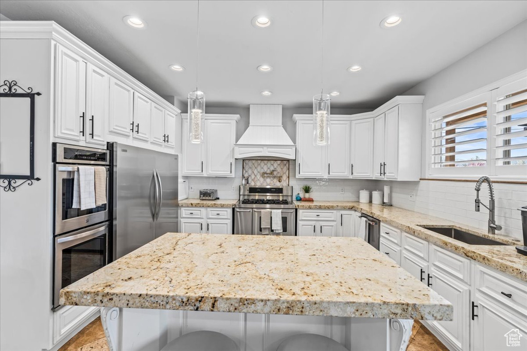 Kitchen featuring a kitchen breakfast bar, premium range hood, white cabinetry, appliances with stainless steel finishes, and sink