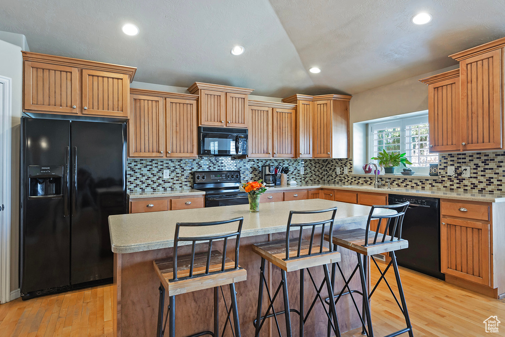 Kitchen with tasteful backsplash, black appliances, a center island, and light hardwood / wood-style flooring
