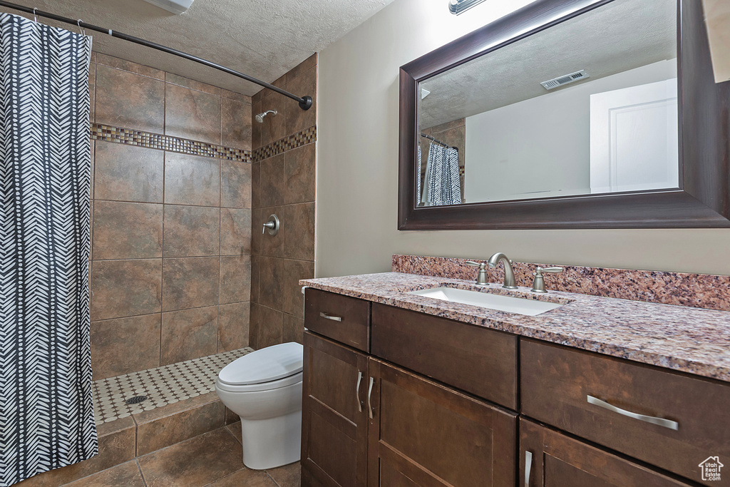 Bathroom with curtained shower, tile floors, toilet, and vanity