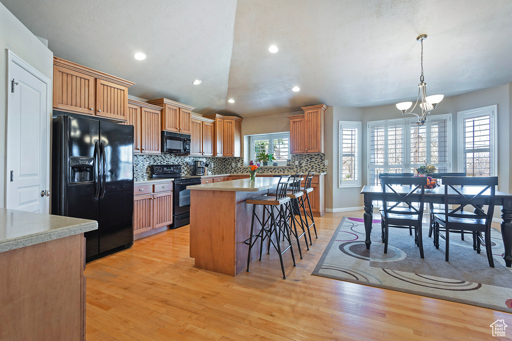 Kitchen featuring a kitchen breakfast bar, hanging light fixtures, light hardwood / wood-style floors, and black appliances