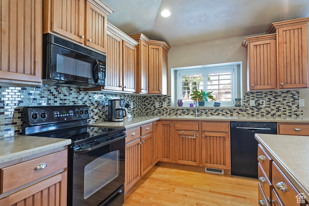 Kitchen with backsplash, light hardwood / wood-style flooring, sink, and black appliances