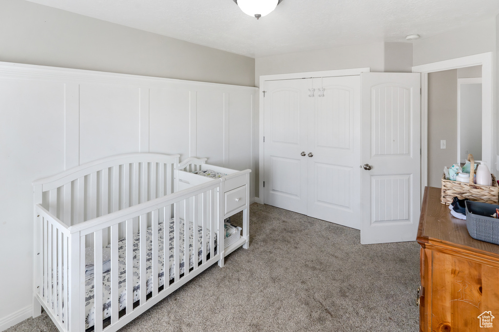 Bedroom featuring light colored carpet, a nursery area, and a closet