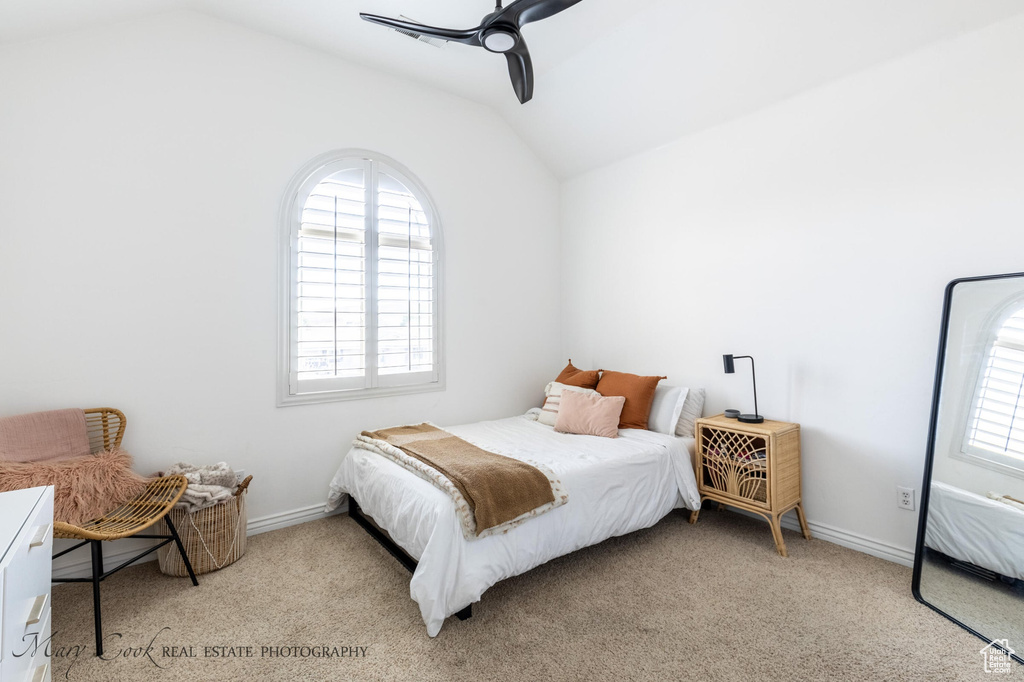 Carpeted bedroom with ceiling fan, vaulted ceiling, and multiple windows