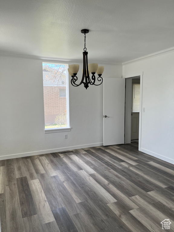 Spare room featuring dark hardwood / wood-style floors, crown molding, and an inviting chandelier