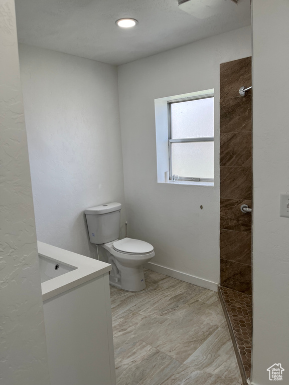 Bathroom with vanity, tiled shower, toilet, and tile flooring