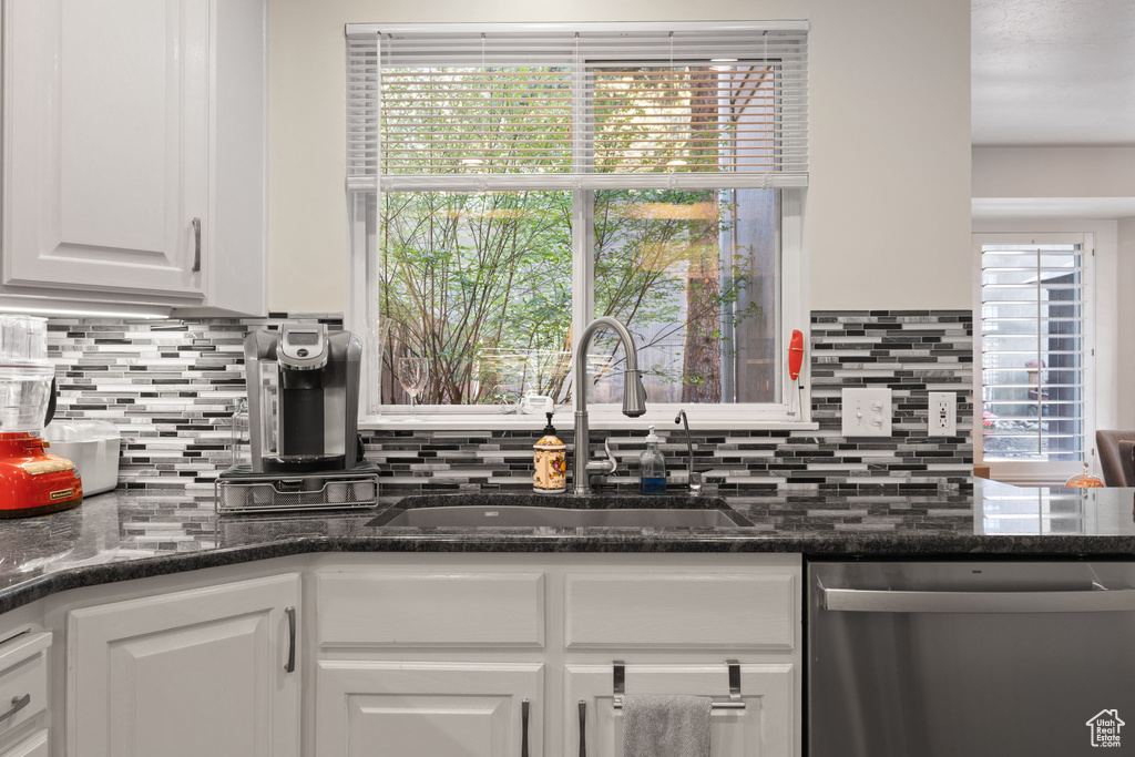 Kitchen featuring backsplash, white cabinetry, dark stone countertops, sink, and stainless steel dishwasher
