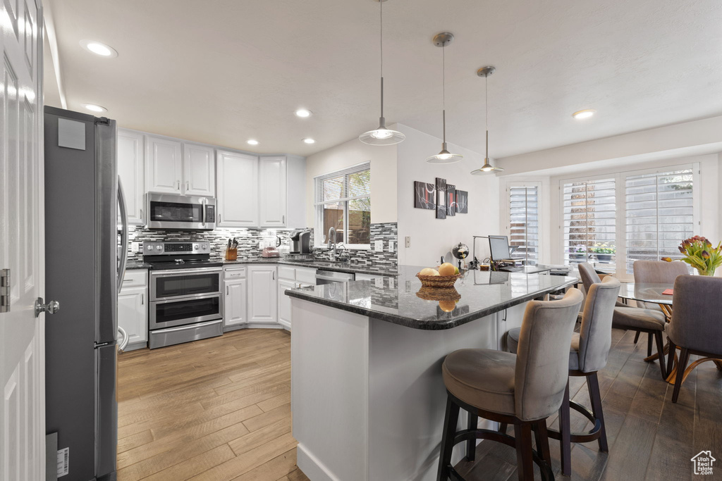 Kitchen featuring appliances with stainless steel finishes, light hardwood / wood-style floors, backsplash, white cabinetry, and hanging light fixtures