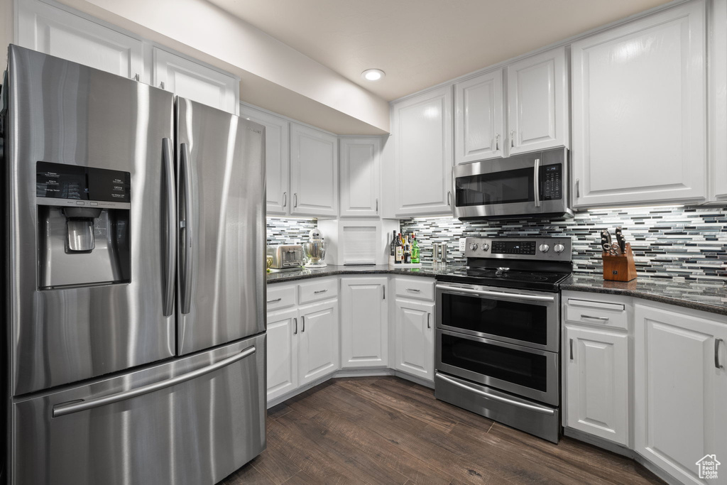 Kitchen featuring appliances with stainless steel finishes, dark hardwood / wood-style floors, tasteful backsplash, and white cabinets