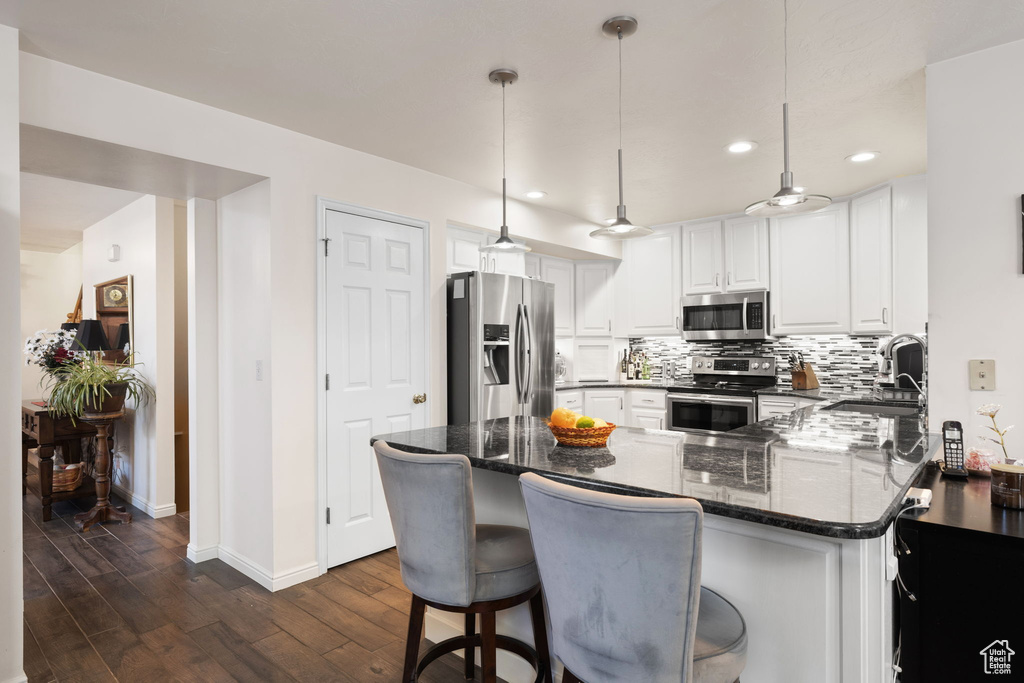 Kitchen with decorative light fixtures, white cabinets, backsplash, stainless steel appliances, and sink