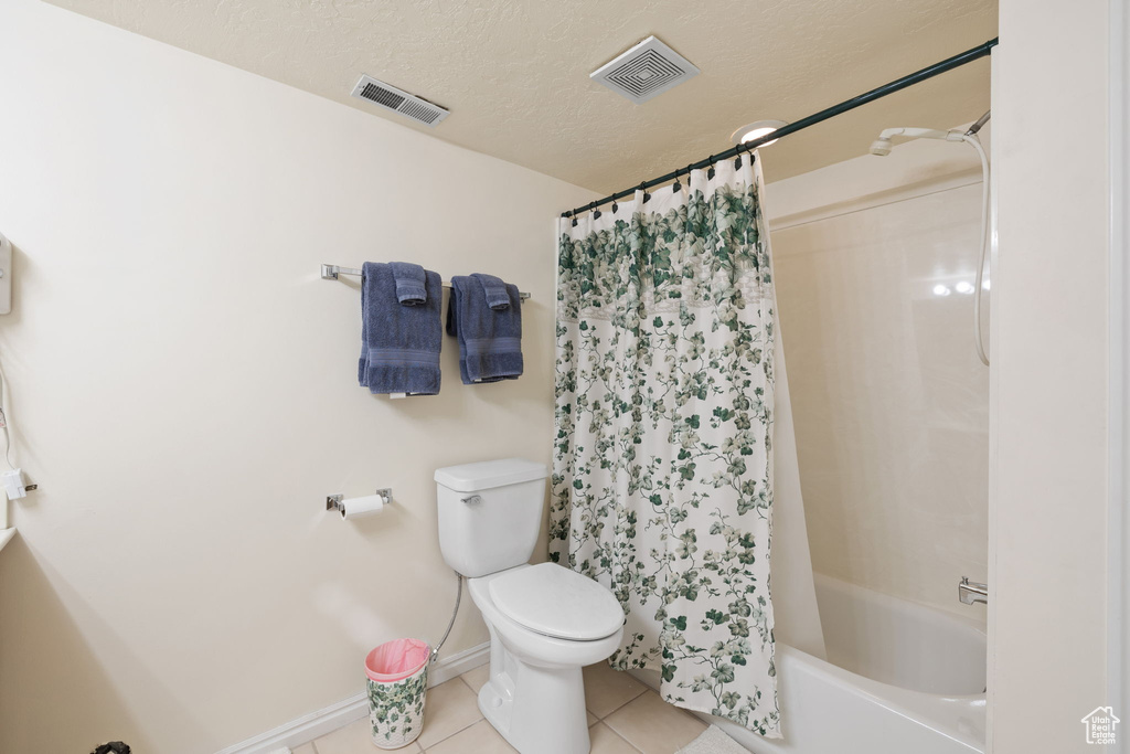 Bathroom featuring a textured ceiling, shower / bathtub combination with curtain, toilet, and tile flooring