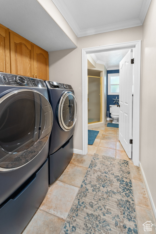 Laundry area featuring crown molding, cabinets, light tile floors, and washing machine and dryer