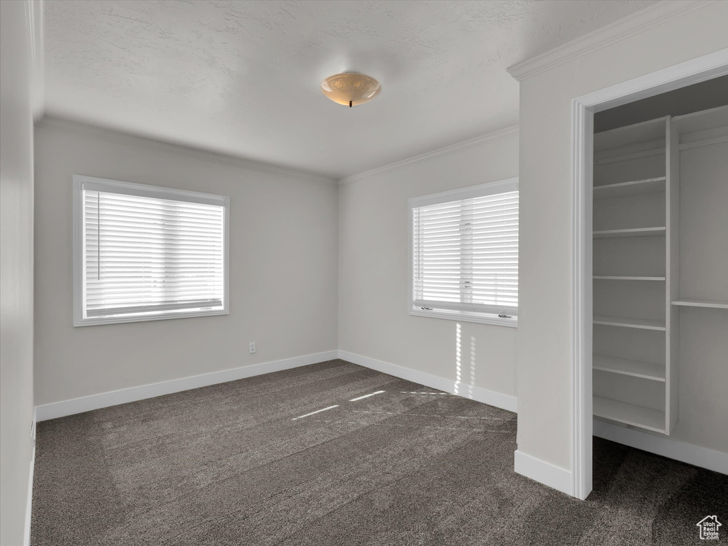 Unfurnished bedroom with ornamental molding and dark carpet