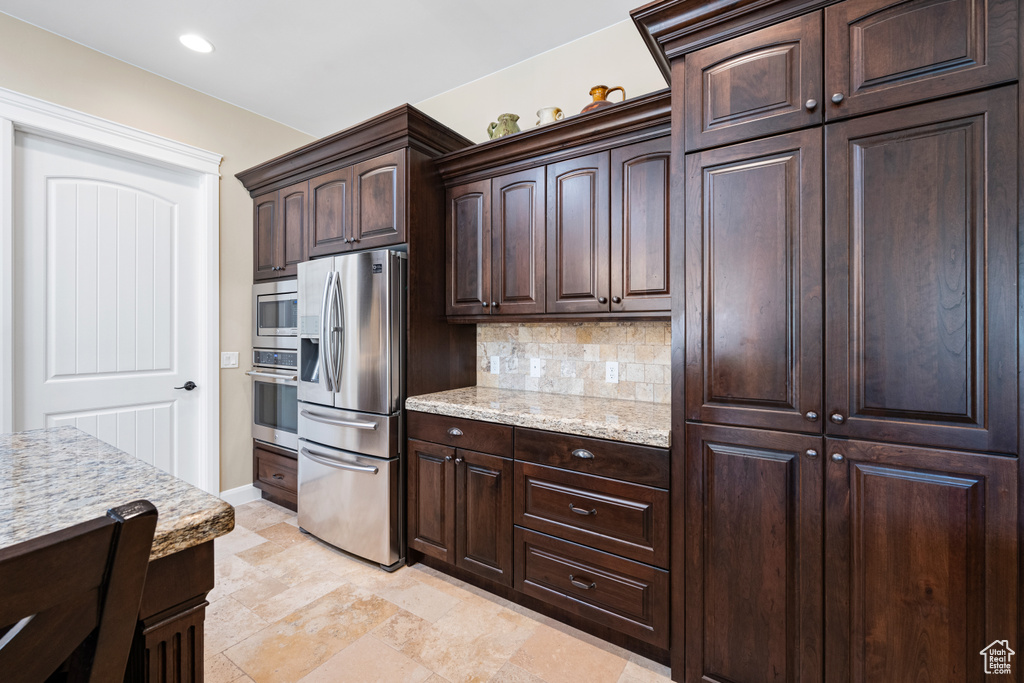 Kitchen featuring dark brown cabinets, light stone countertops, stainless steel appliances, tasteful backsplash, and light tile floors