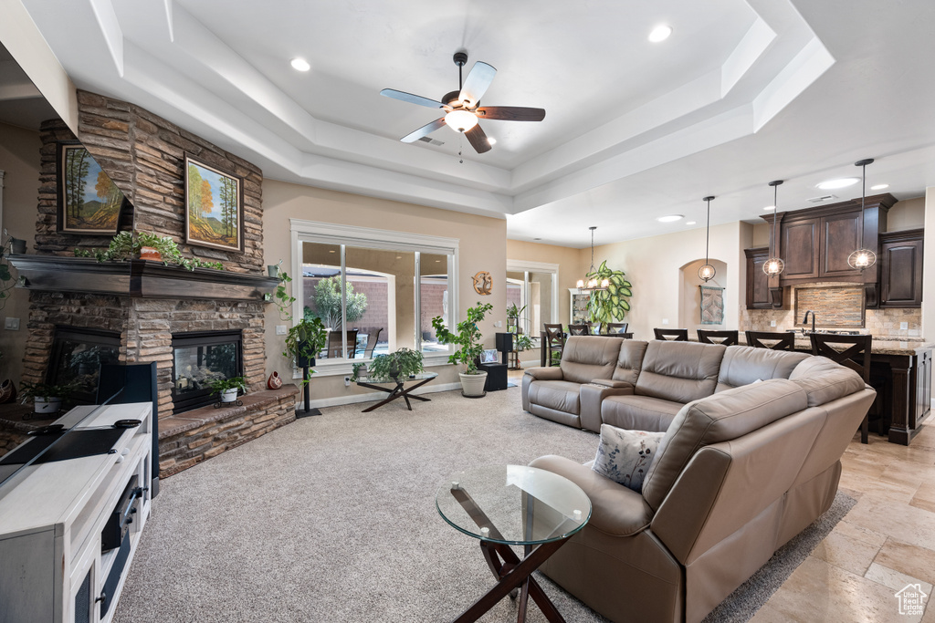Living room with ceiling fan, a tray ceiling, light tile flooring, and a stone fireplace